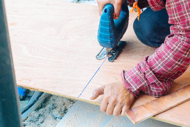 建設現場で大きな木板を切るために電気のこぎりを使ってアジアの男性大工をクローズアップ。男性労働者の鋸のボード。職人ワークショップルーチン。手作りとクラフト家具のコンセプト. - 写真・画像