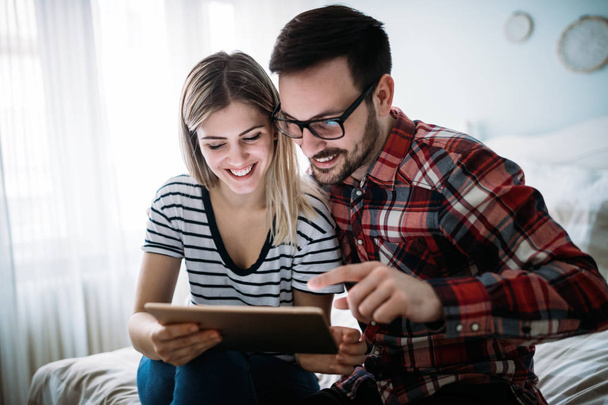 Young happy couple using digital tablet in bedroom - 写真・画像