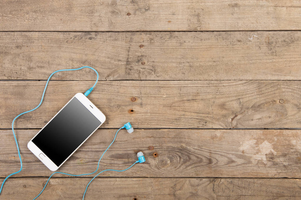 Bílý smartphone se sluchátky na staré dřevěné desce - Fotografie, Obrázek