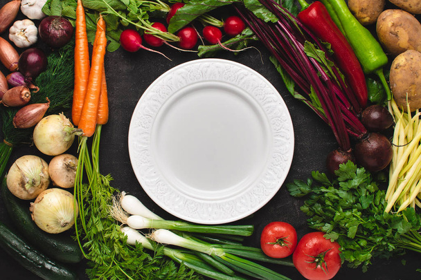 Üres fehér lemez mockup friss zöldségekkel. Vegetáriánus nyers élelmiszer. Az egészséges étkezés fogalma a másolási tér. - Fotó, kép