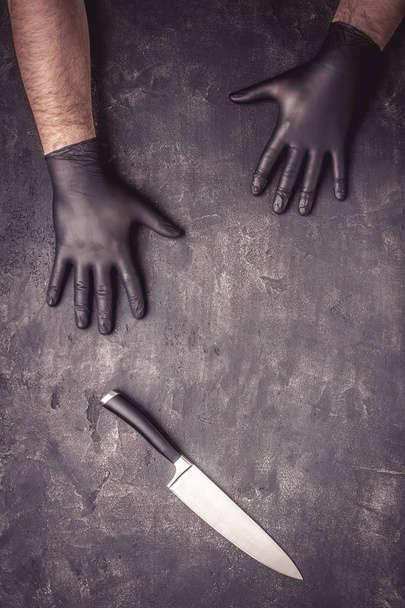 Grote mes en mannelijke handen met zwarte latex handschoenen op donkere achtergrond - Foto, afbeelding