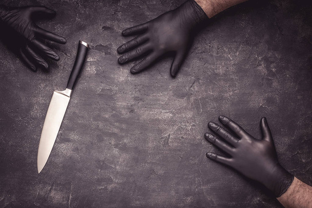 Mains masculines avec gants en latex noir et couteau sur fond foncé
 - Photo, image