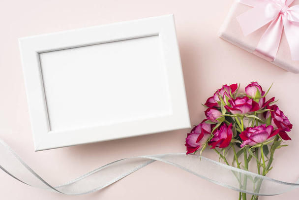 Bunch of red roses, wooden frame, gift box and ribbon on pink background. - 写真・画像