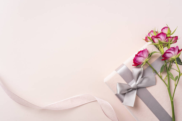 Κόκκινα τριαντάφυλλα με κουτί δώρου και κορδέλα σε ροζ φόντο με χώρο αντιγραφής - Φωτογραφία, εικόνα