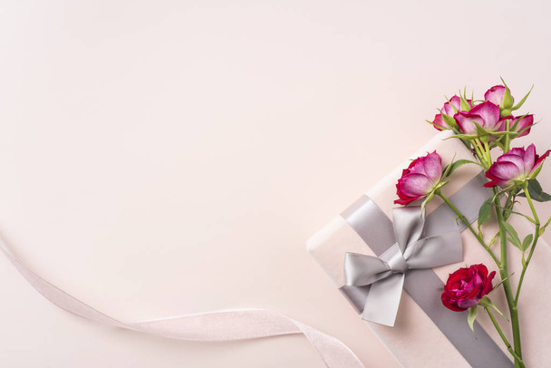 Strauß roter Rosen, Schleife und Geschenkbox auf rosa Hintergrund zum Muttertag - Foto, Bild
