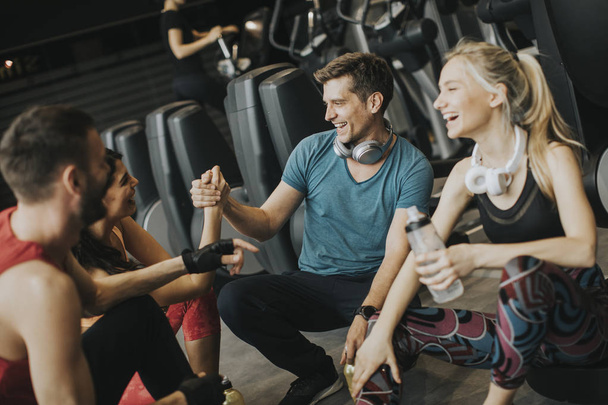 Groupe pf jeunes en vêtements de sport parler et rire ensemble tout en se reposant dans la salle de gym après une séance d'entraînement
 - Photo, image