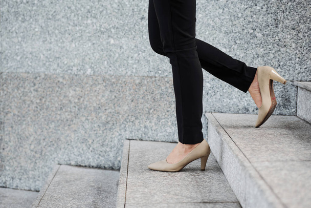 Πόδια της νεαρής γυναίκας με μαύρο τζιν και γυμνά τακούνια περπάτημα κάτω σκάλες - Φωτογραφία, εικόνα