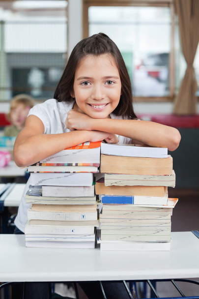 Schoolgirl Leaning On Stacked Books At Desk - Zdjęcie, obraz