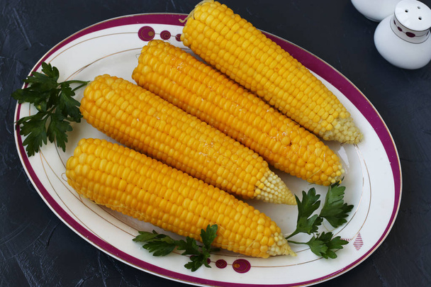 Gotowane kukurydza znajduje się na talerzu na ciemnym tle, widok z góry - Zdjęcie, obraz