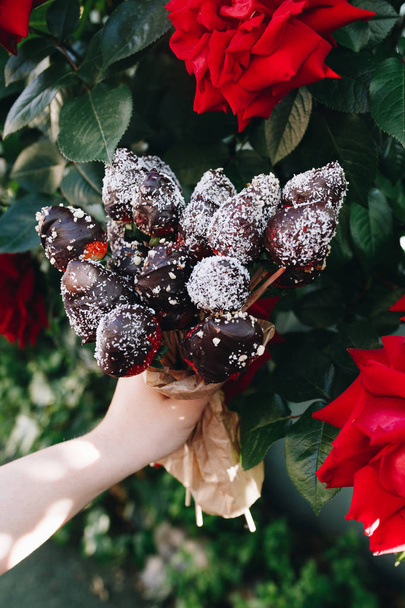 Un bouquet de fraises recouvertes de chocolat gros plan de roses rouges avec différentes garnitures : chocolat noix de coco cacao amandes noix
 - Photo, image