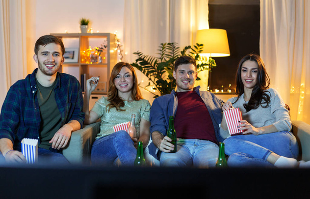 friends with beer and popcorn watching tv at home - Fotó, kép