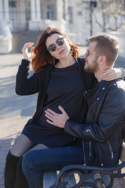 A couple in love, a man and a pregnant woman, walk together in the spring in a beautiful sunny city.Pregnant woman and man hug each other and show their love. Happy couple is expecting a baby. The concept of love and family well-being - Fotoğraf, Görsel