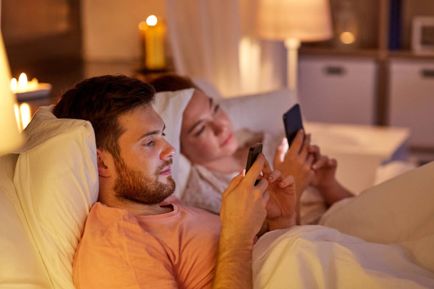 couple using smartphones in bed at night - Fotó, kép