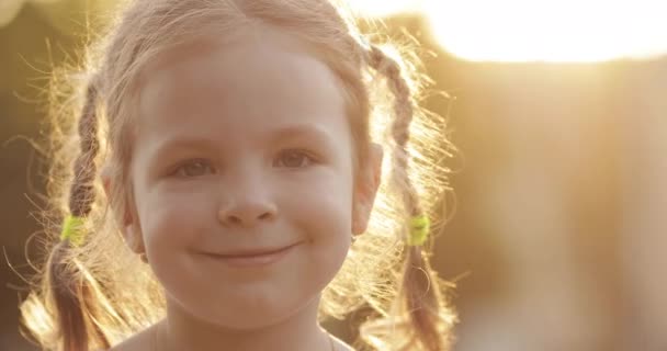 Υπέροχο μικρό κορίτσι χαμογελά στην κάμερα με οπίσθιο φωτισμό φως του ήλιου. - Πλάνα, βίντεο