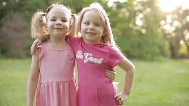 Cute young children in pink dresses hugging and smiling at camera in park. - Footage, Video