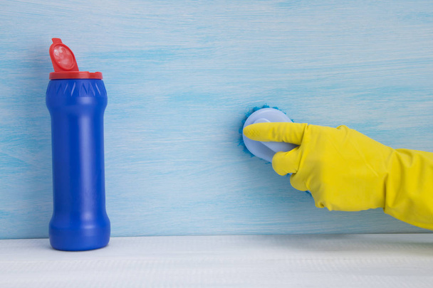 青い背景に、黄色い手袋の手が表面をブラシで、洗浄粉末のボトルの隣に、書く場所があります - 写真・画像