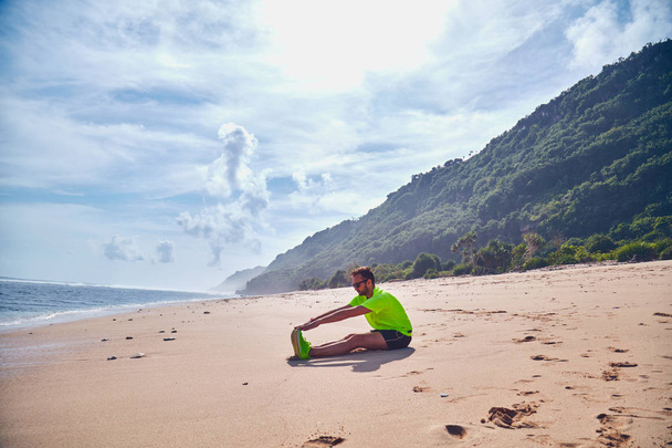 Спортсмен розтягується на екзотичному тропічному пляжі після бігу /
  - Фото, зображення