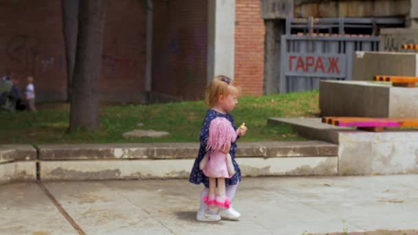 Ένα μικρό ξανθό κορίτσι με ένα μπλε φόρεμα απολαμβάνει τα περιστέρια - Πλάνα, βίντεο