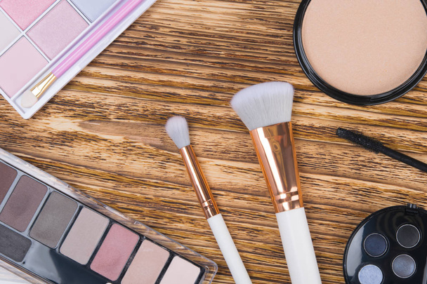 close-up, on a wooden background, colorful makeup shadows, white brushes and powder to improve the complexion - Photo, image