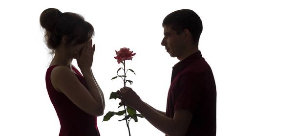 silhueta de um jovem casal apaixonado no fundo isolado branco, o homem dá uma flor de rosa a uma mulher, amor conceito
 - Foto, Imagem