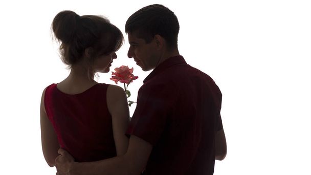 silhouette profile of a young couple sensually bowed their heads to the bud of a rose on white isolated background, boy and girl in romance, concept love - Фото, изображение