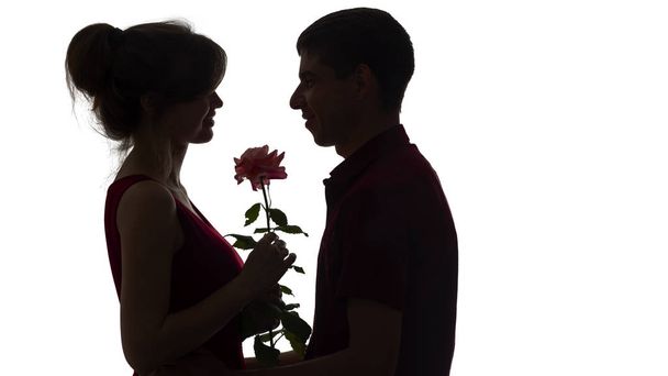 silhouette of a young couple in love on white isolated background, man gives a woman a rose flower, concept love - Photo, image