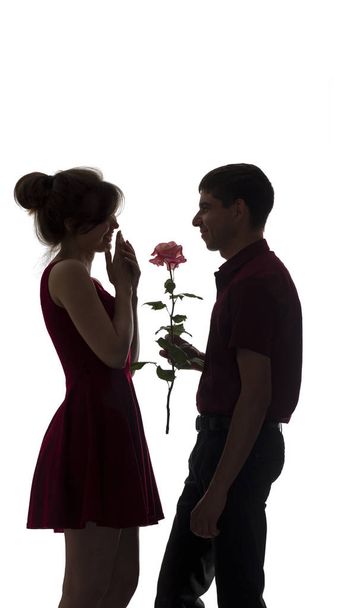 silhouette of a young couple in love on white isolated background, man gives a woman a rose flower, concept love - Zdjęcie, obraz