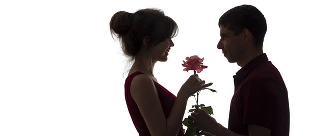 silhouette profile of a young couple in love on white isolated background, man giving a woman a rose flower, girl is delighted with the care of a guy, concept romance - Photo, image