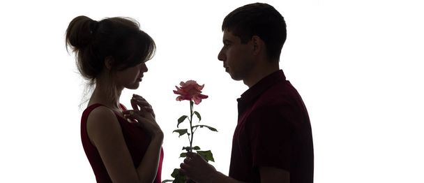 silhouette profile of a young couple in love on white isolated background, man giving a woman a rose flower, concept love and romance - Photo, image
