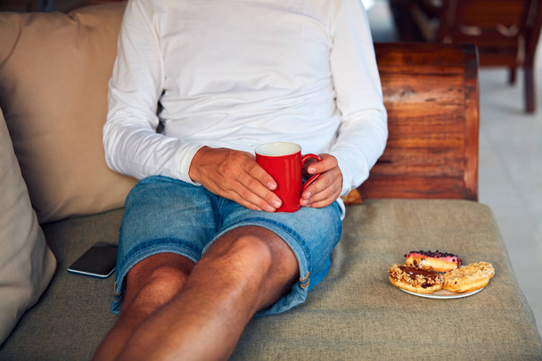 Uomo seduto su un divano terrazza e bere caffè / tè, mangiare fare
 - Foto, immagini