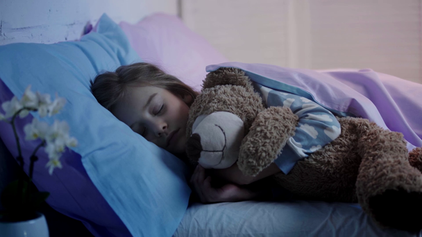 χαριτωμένο παιδί με αρκουδάκι κοιμάται στο κρεβάτι, ενώ το φως απενεργοποίηση - Πλάνα, βίντεο