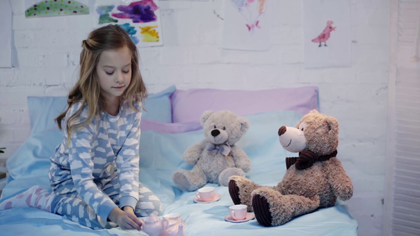garoto bonito em pijama sentado na cama e brincando com brinquedos no quarto
 - Filmagem, Vídeo