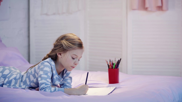 koncentruje Cute dziecko w piżamie leżącego na łóżku i rysunek z ołówków kolorowych - Materiał filmowy, wideo