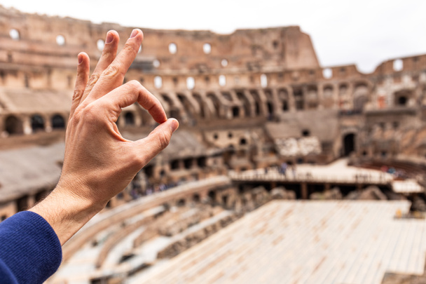 ROME, ITALY - JUNE 28, 2019: cropped view of man showing okay sign in front of Colosseum - Foto, imagen