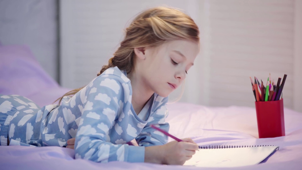 koncentruje Cute dziecko w piżamie leżącego na łóżku, rysunek i zmieniające się kredki kolor - Materiał filmowy, wideo