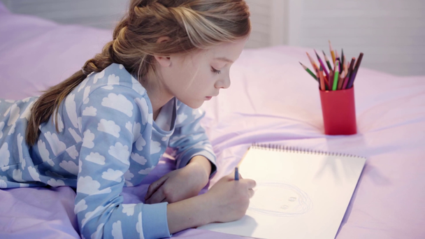 cute child in pajamas lying on bed and drawing with color pencils - Footage, Video