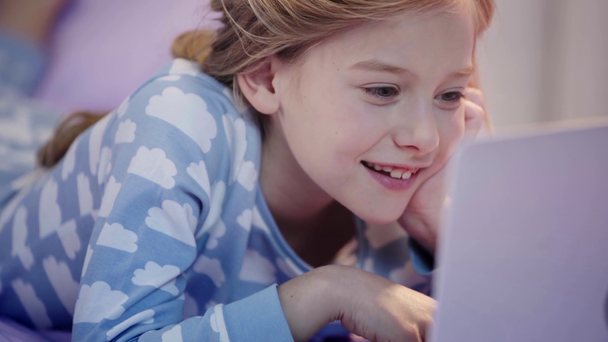 enfant préadolescent en pyjama couché sur le lit, en utilisant un ordinateur portable et le visage d'appui avec la main avec le sourire
 - Séquence, vidéo