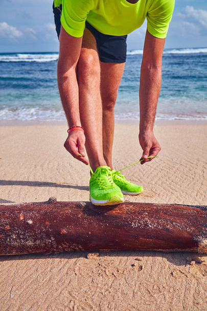 Чоловік зав'язує кросівки на тропічному екзотичному пляжі
. - Фото, зображення