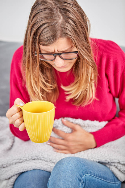 Ragazza malata in possesso di tazza e bere caffè / tè su un divano
. - Foto, immagini