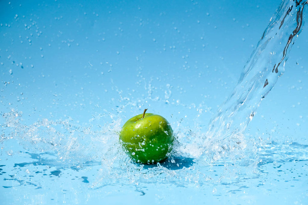 Green apples in clear water splash on blue background - Foto, Imagem