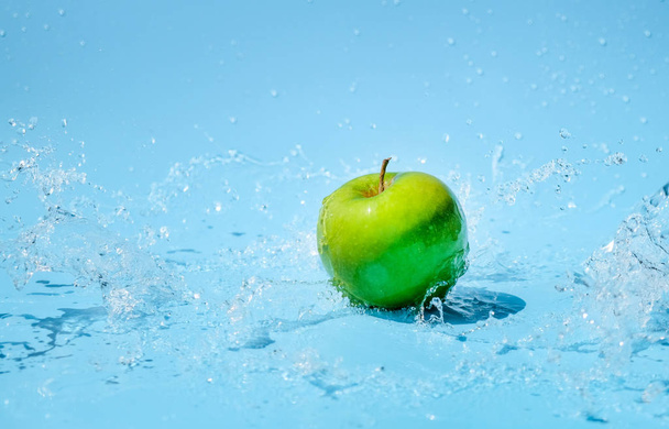 Green apples in clear water splash on blue background - 写真・画像