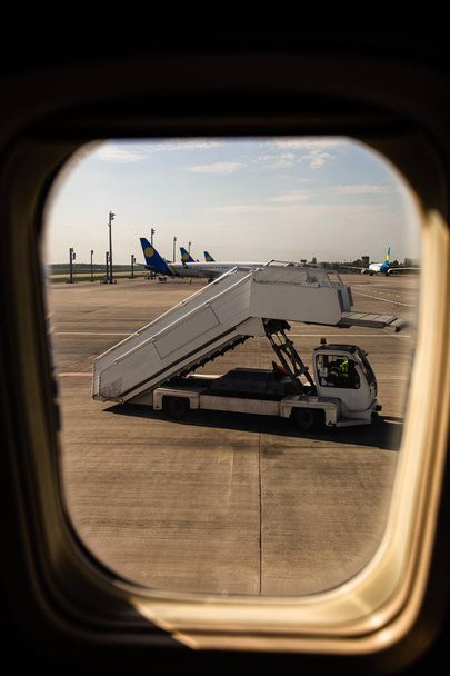 ROME, ITALY - JUNE 28, 2019: airplanes and ground support equipment behind plane window in rome, italy - Foto, imagen