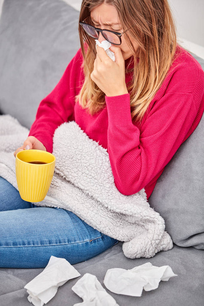 Chora dziewczyna trzyma filiżankę i picie kawy/herbaty na kanapie. - Zdjęcie, obraz