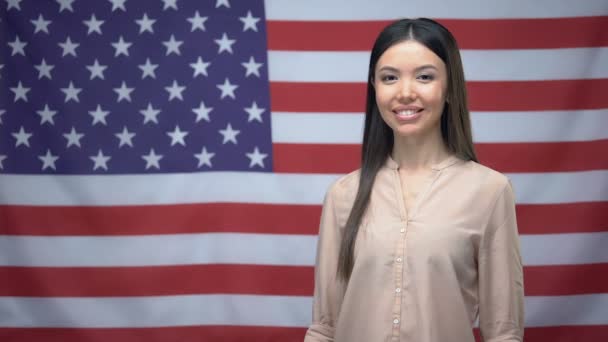 Mulher asiática feliz mostrando polegares para cima e piscar contra o fundo da bandeira dos EUA
 - Filmagem, Vídeo