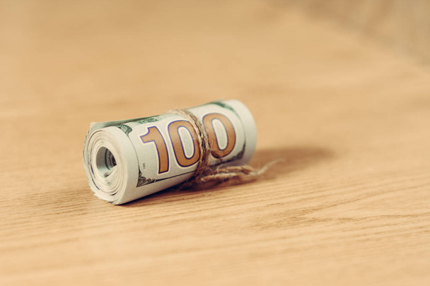 A roll of a hundred dollar bills on a light brown background. - Foto, Imagem
