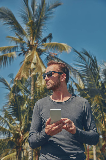 Hombre usando teléfono celular / smartphone en ambiente tropical
. - Foto, Imagen