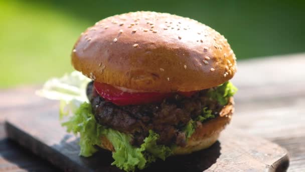 leckere Rindfleisch-Burger mit Salat, Zwiebeln und Tomaten serviert Garten im Freien - Filmmaterial, Video