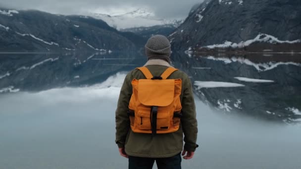 Hiker enjoying the snowy mountain peaks view. Low-angle back view of male hiker with yellow backpack and enjoying the view of snowy mountain peaks - Footage, Video