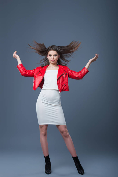 Fashionable style, fashion women's clothing, color combination. Beautiful brunette girl in white dress and red leather jacket. Flying hair - Zdjęcie, obraz