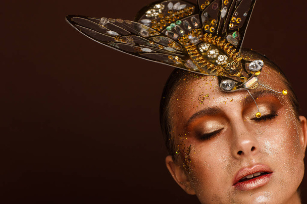 Portrait of a beautiful woman with expressive creative make-up in bronze and with a decoration on her head - Photo, Image